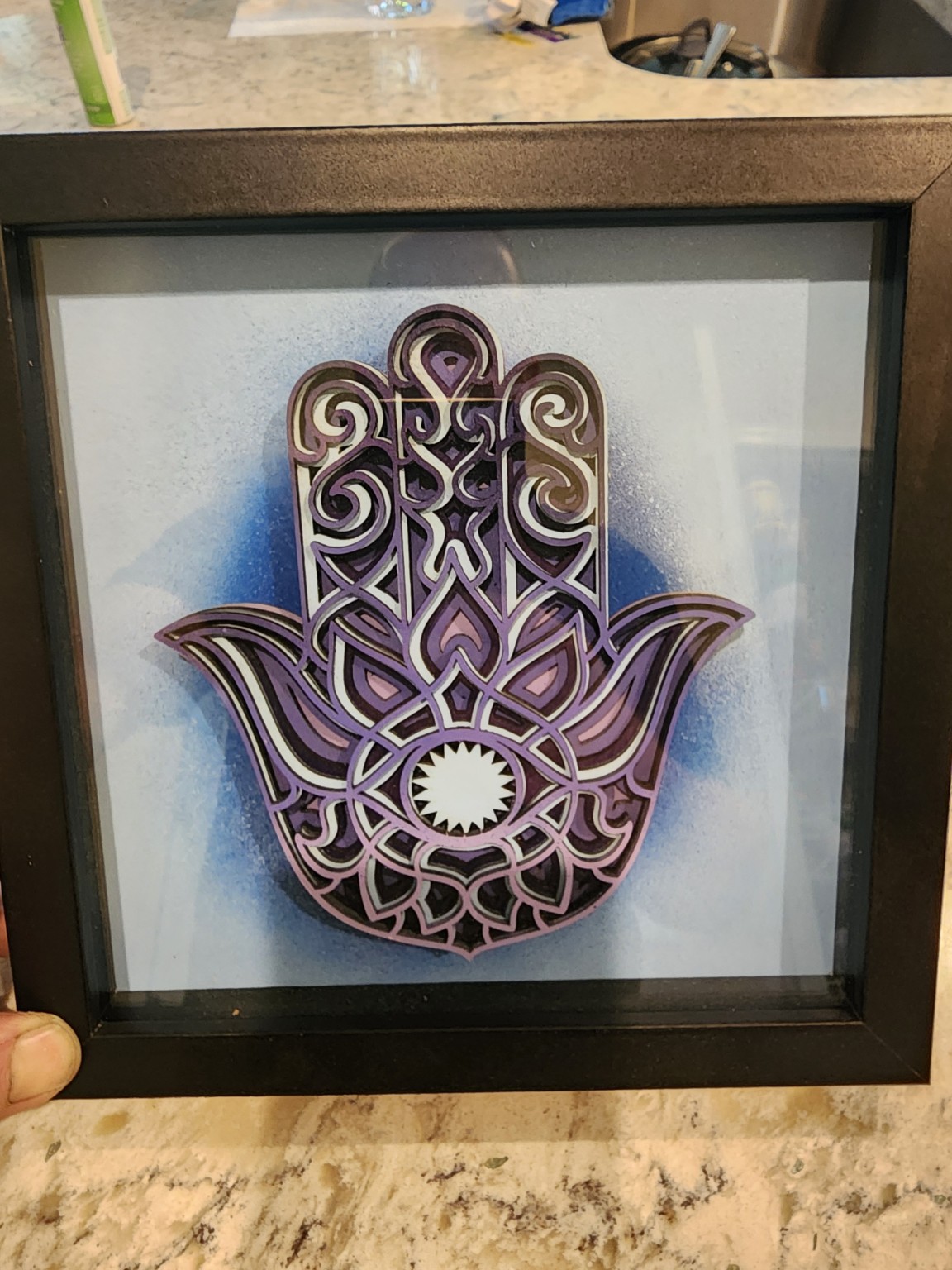 Purple layered hamsa hand artwork in a black frame